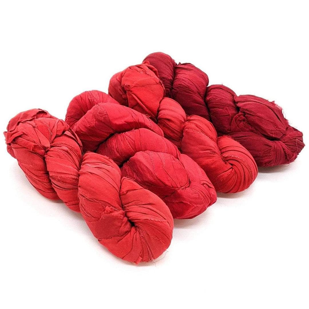 4 skeins of red ombre ribbon yarn on a white background
