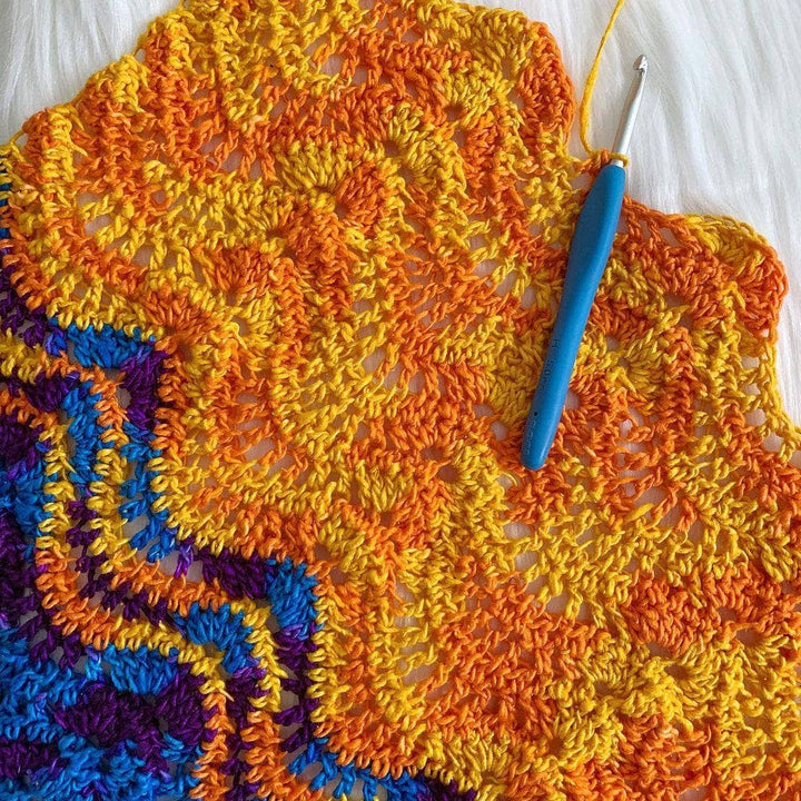 Ombre silk yarn in orange worked up into a crochet pattern of wavy chevrons in front of a fuzzy white background.