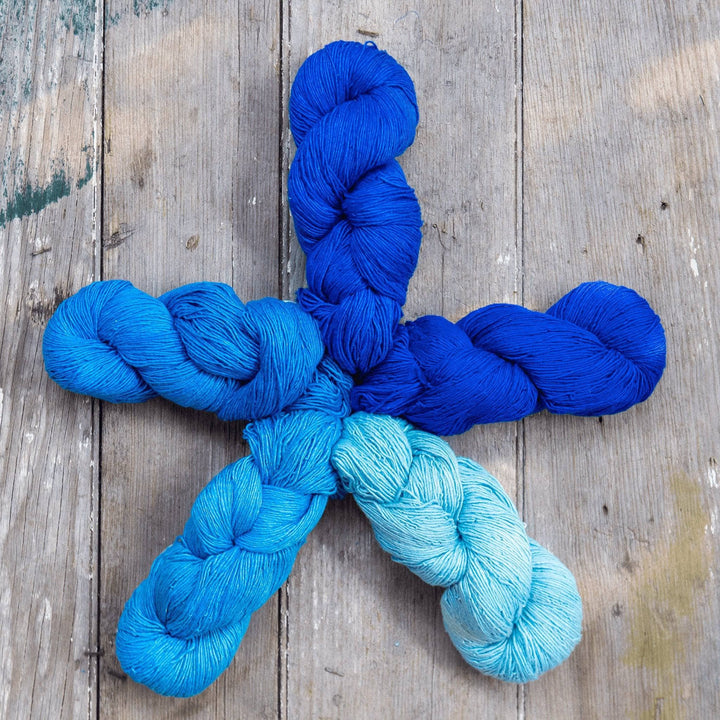 5 skeins of sport weight silk yarn arranged in a star shape in front of a wood background. Skeins are each a slightly different shade than the next to create an ombre or fade effect.
