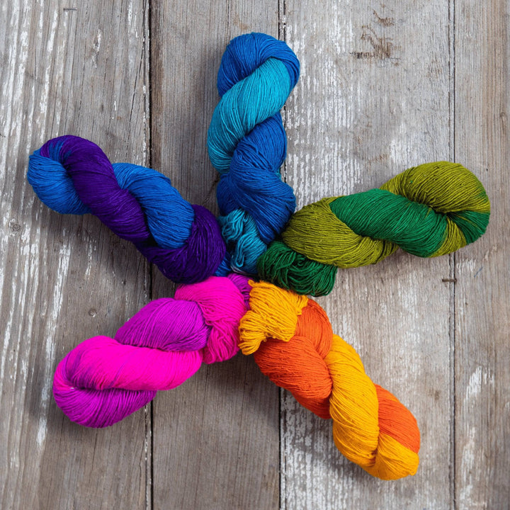 5 skeins sport weight silk yarn arranged in a star formation in front of a wood background. Skeins are ombre giving the yarn a variegated effect. Clockwise starting from 12 is light blue, green, orange, pink, and dark blue.