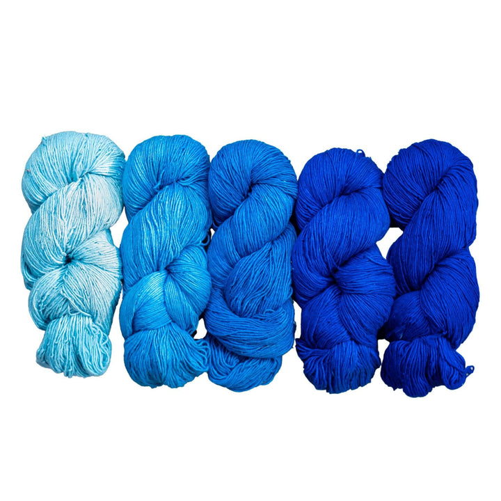 5 skeins sport weight silk in the colorway blues in front of a white background. From left to right are lightest to darkest blue in this ombre or fade pack.