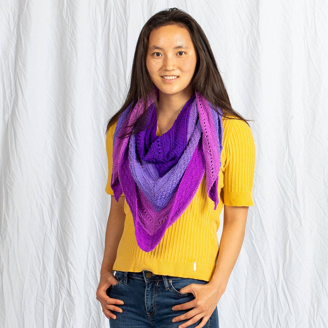 model wearing ombre stitch sampler shawl around their neck in front of a white background.