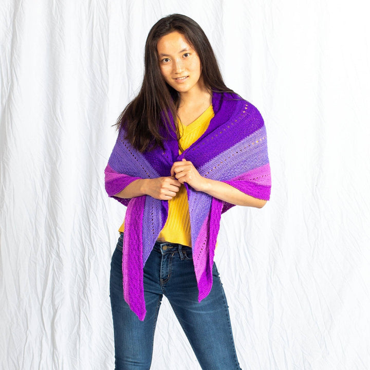 Model wearing ombre stitch sampler shawl in purple in front of a white background.
