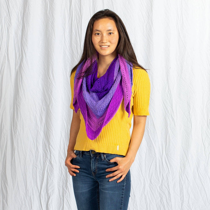 Model wearing ombre stitch sampler shawl in purple around their neck in front of a white background.