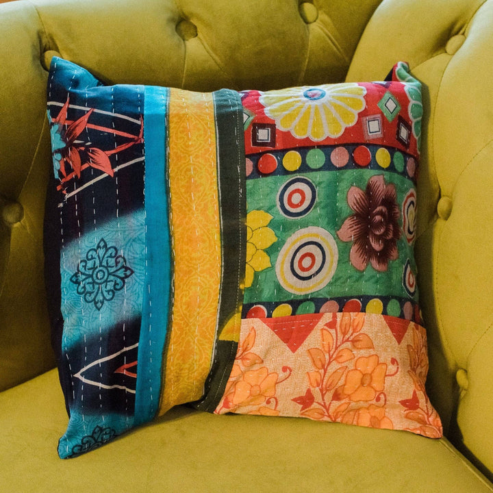 Kantha pillow cover sitting in the corner of a green velvet couch. 