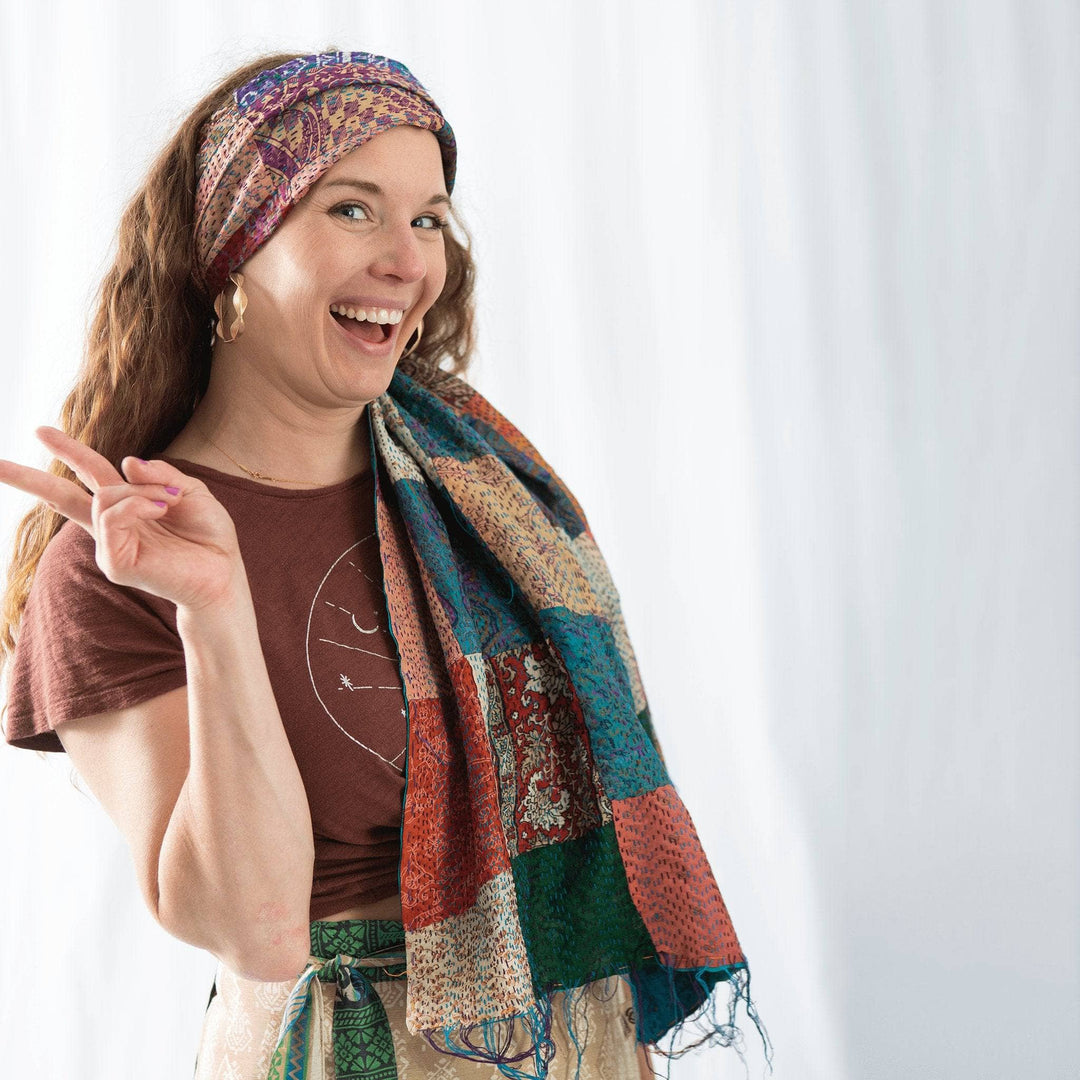 Founder nicole wearing a neutral multicolor kantha scarf as a headband while making peace sign with right hand in front of a white background.