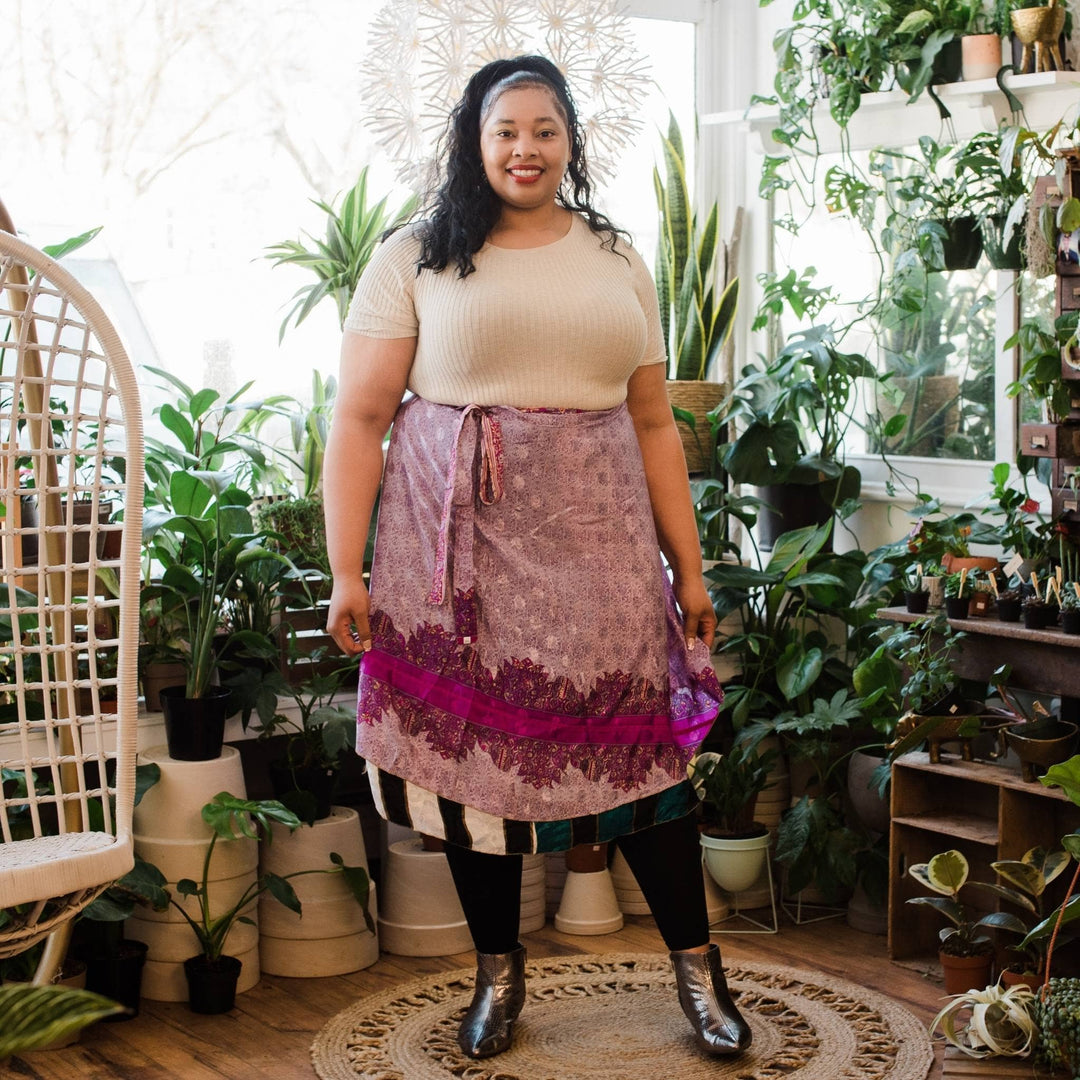 Model is wearing a one of a kind pink and purple goddess mini sari wrap skirt with potted plants in the background. 