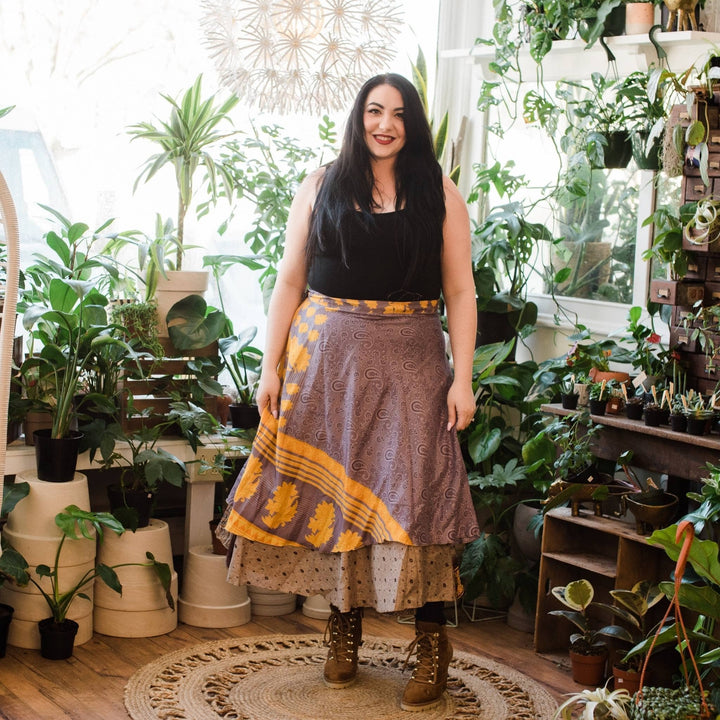 Model is wearing one of a kind purple and gold goddess tea length sari wrap skirt with potted plants in the background.  
