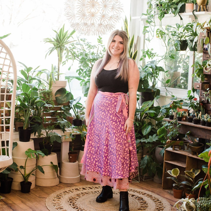 Model is wearing one of a kind pink long sari wrap skirt with potted plants in the background. 
