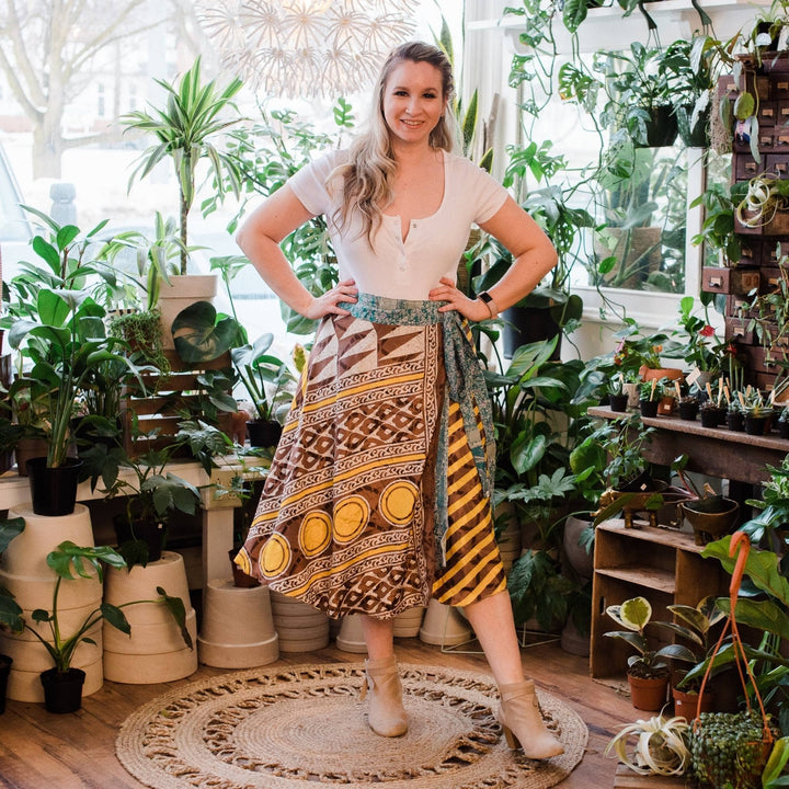 Model is wearing one of a kind yellow and brown tea length sari wrap skirt with potted plant background. 