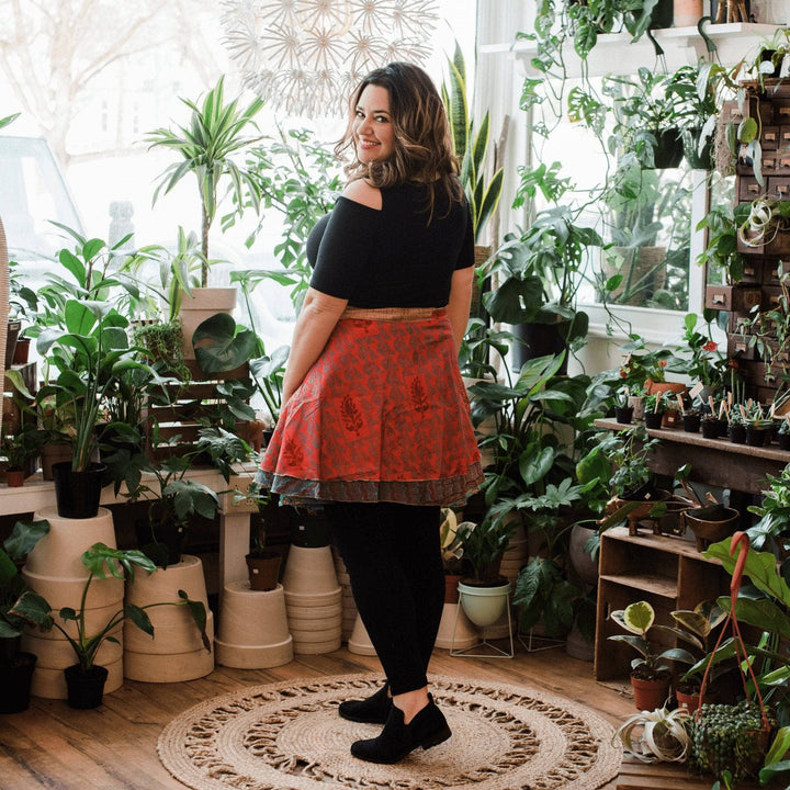 Model wearing one of a kind orange and gold mini sari wrap skirt with potted plants in the background. 