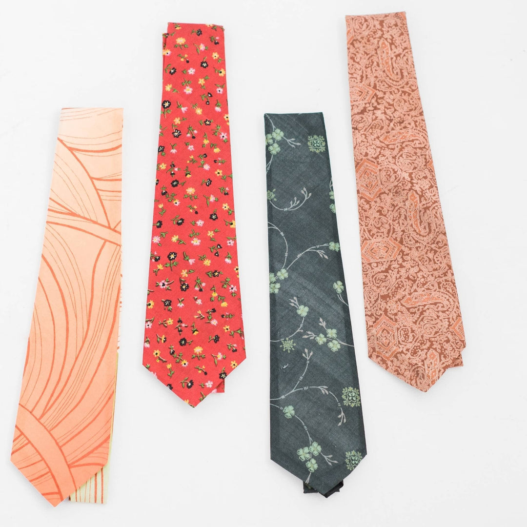 four sari silk neck ties laid out on a white backdrop. From left to right;  orange swirls, red florals, green floral and brown paisley. 