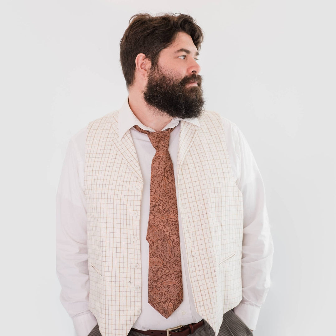 model is standing in front of a white backdrop wearing a brown-ish orange sari silk neck tie. 