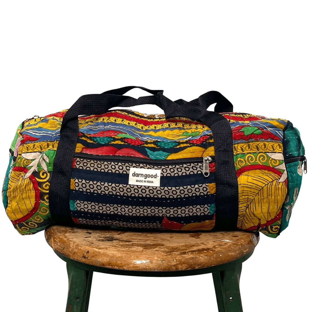 A Kantha Stitched Travel Bag sitting on a wooden stool.