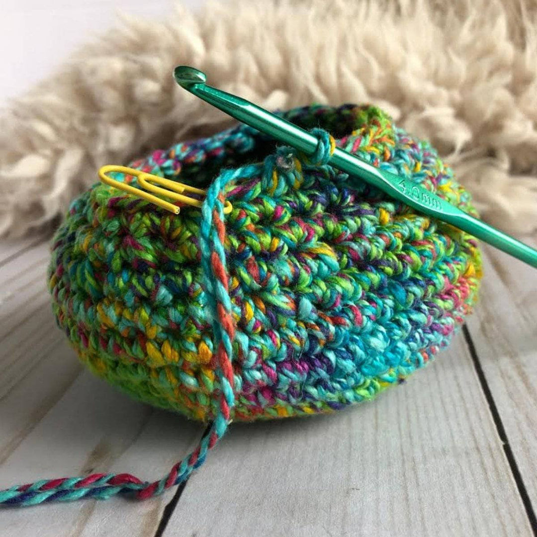 close up of a green hook with yarn on top of a table