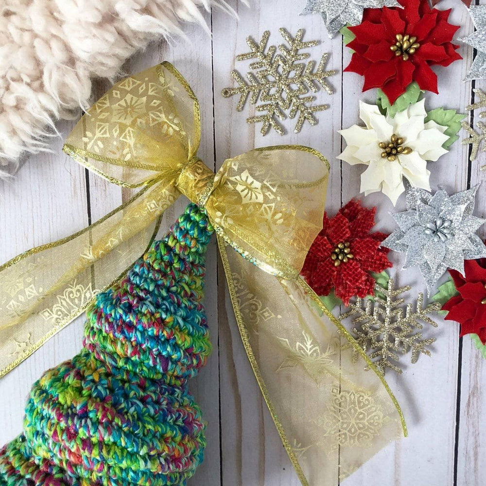 crochet Christmas Tree with a golden bow on top a white table with christmas flowers
