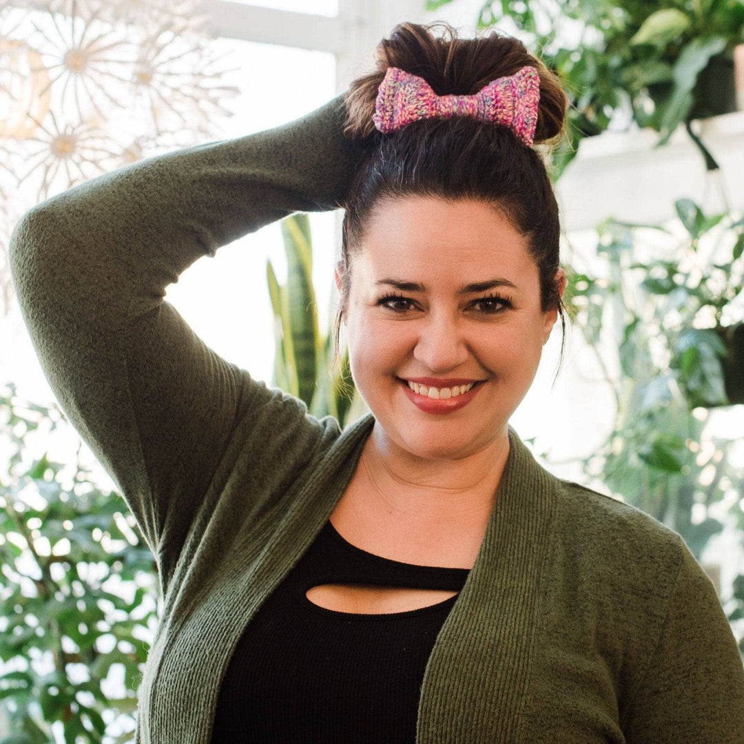 Model wearing party animal bow tie in bun on top of head with potted greenery in the background.