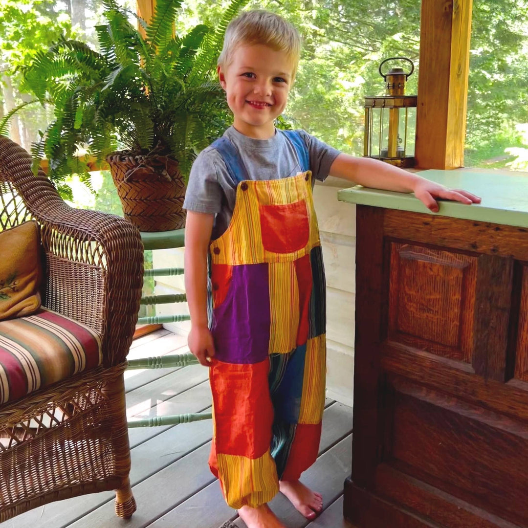 Model is standing outside on a porch wearing yellow and orange patchwork play pants in the large size. 