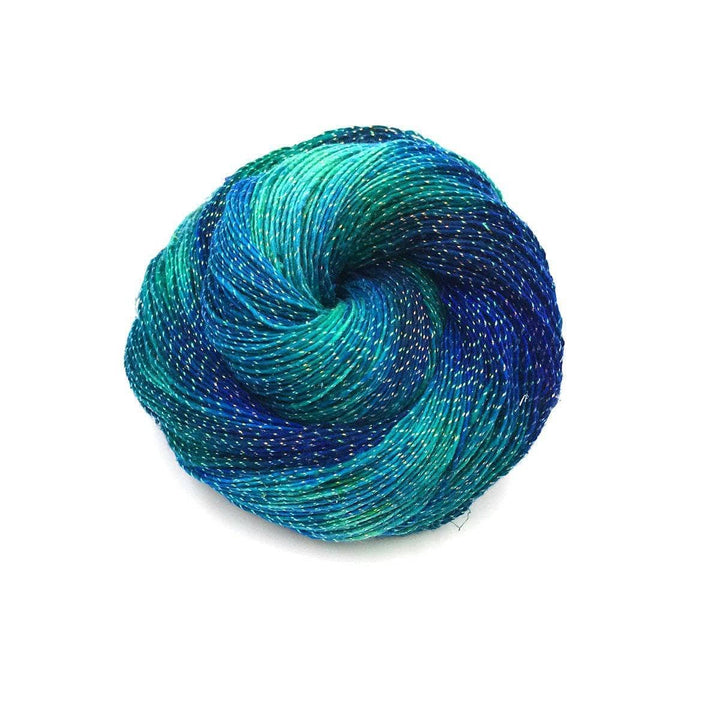 cake of yarn in the color sparkle enchanted forest (green and blue) with a white background