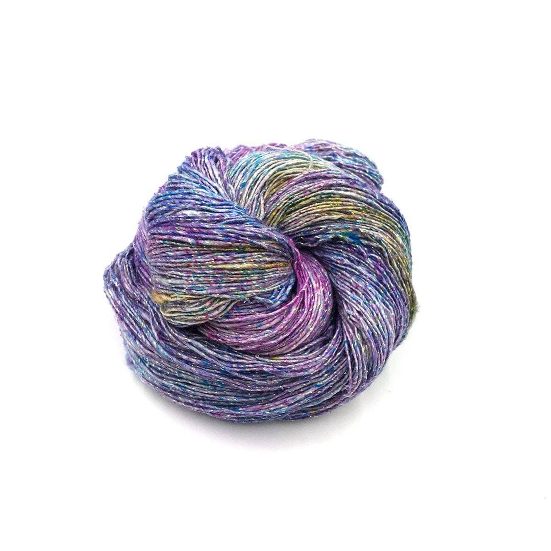 cake of yarn in the color sparkle tidal pool (purple ombre) with a white background