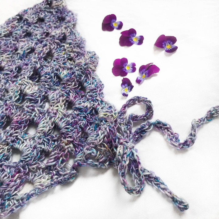close up of a purple beanie made out of yarn with a white background