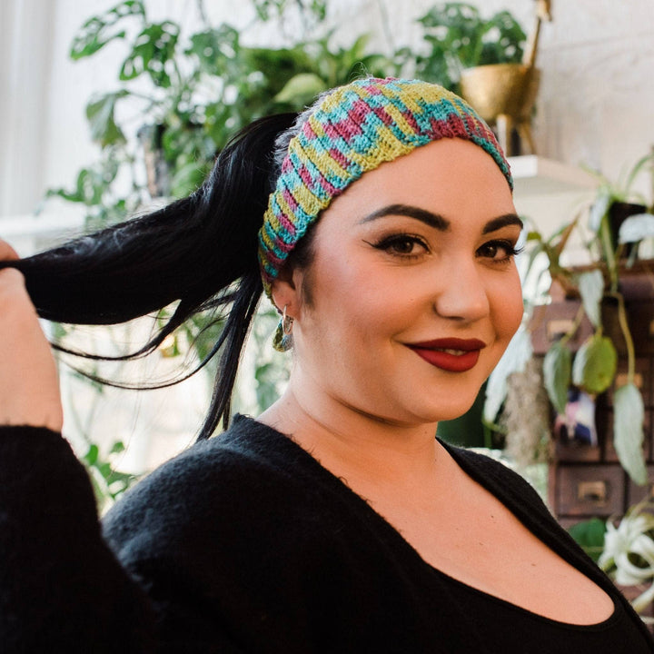 Model wearing plume headband (out of stock colorway) with potted greenery in the background.
