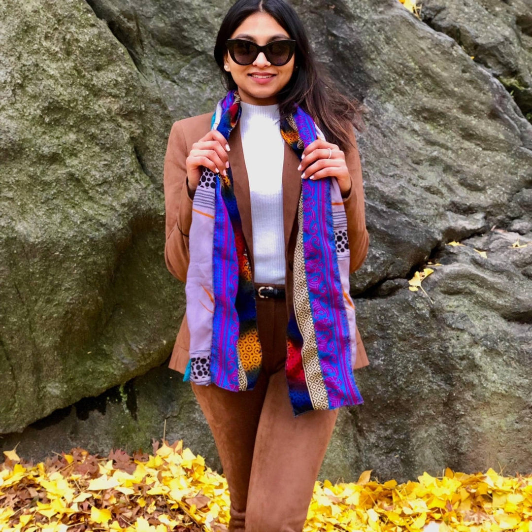 Model is standing outside on fall leaves in front of a big rock wearing a purple sari silk medley scarf. 