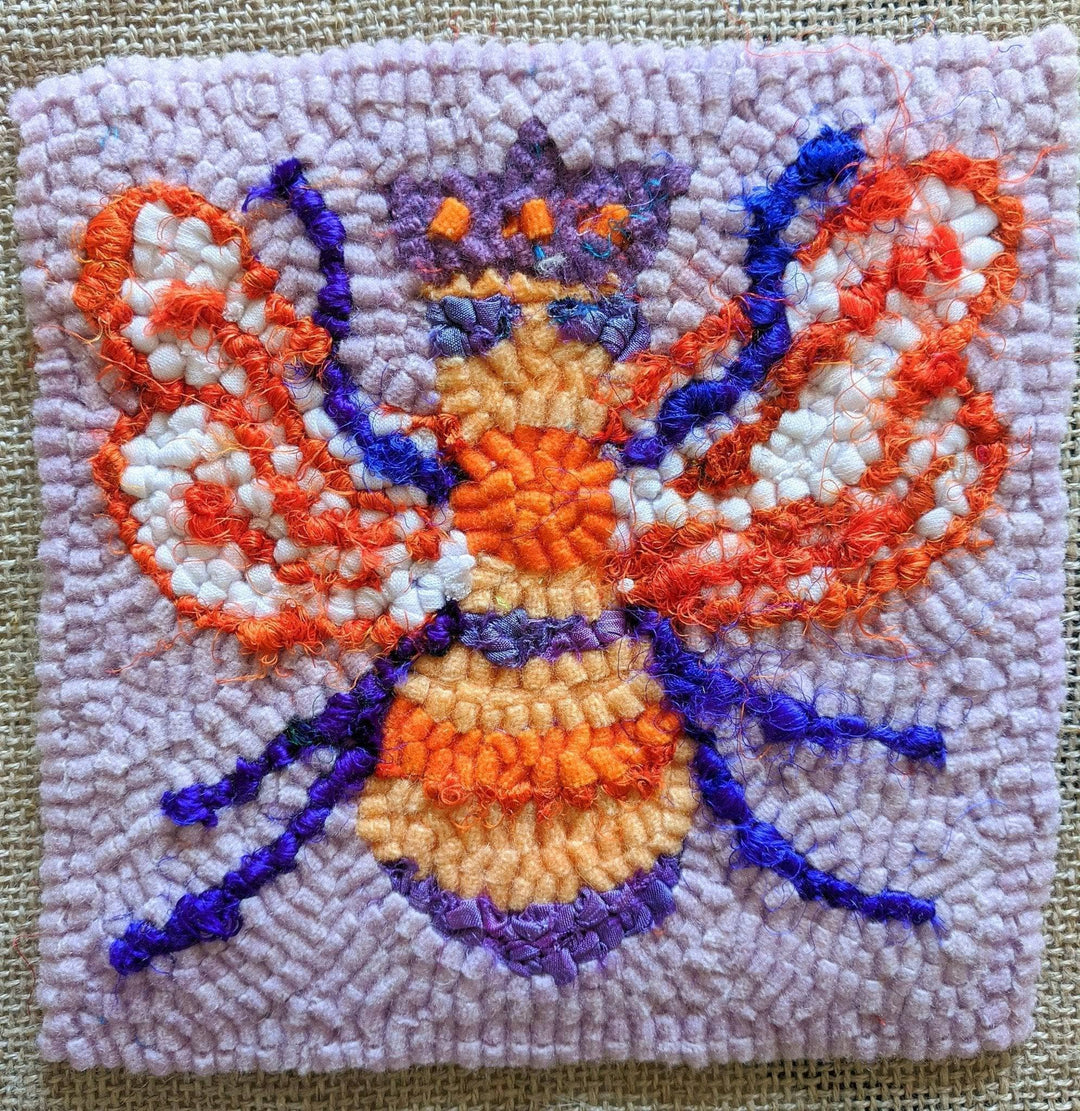 completed queen bee rug hooking kit in front of a canvas background.