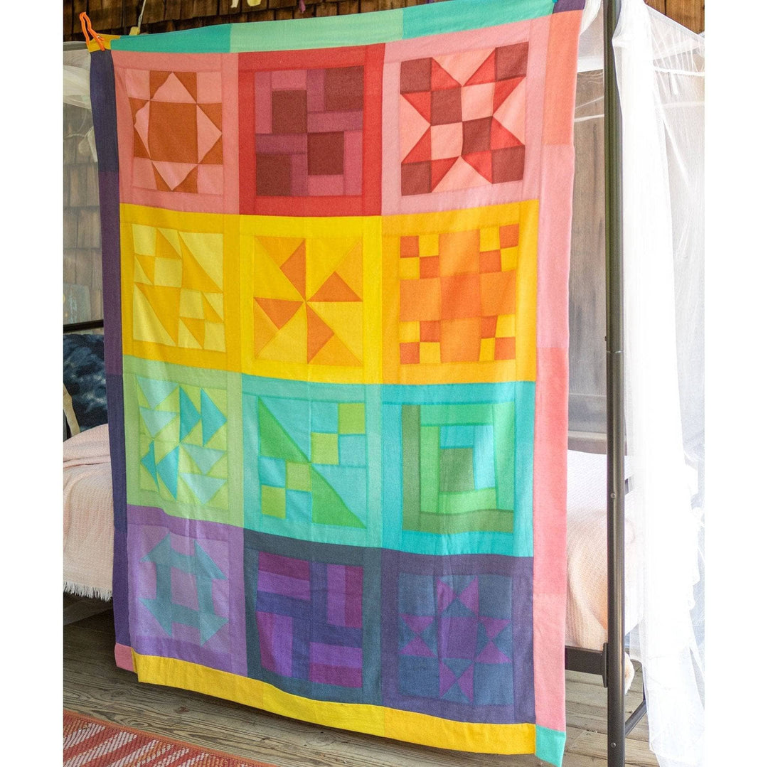 Rainbow Quilt top kit fully assembled and hanging from a canopy bed to display all 12 quilt blocks.