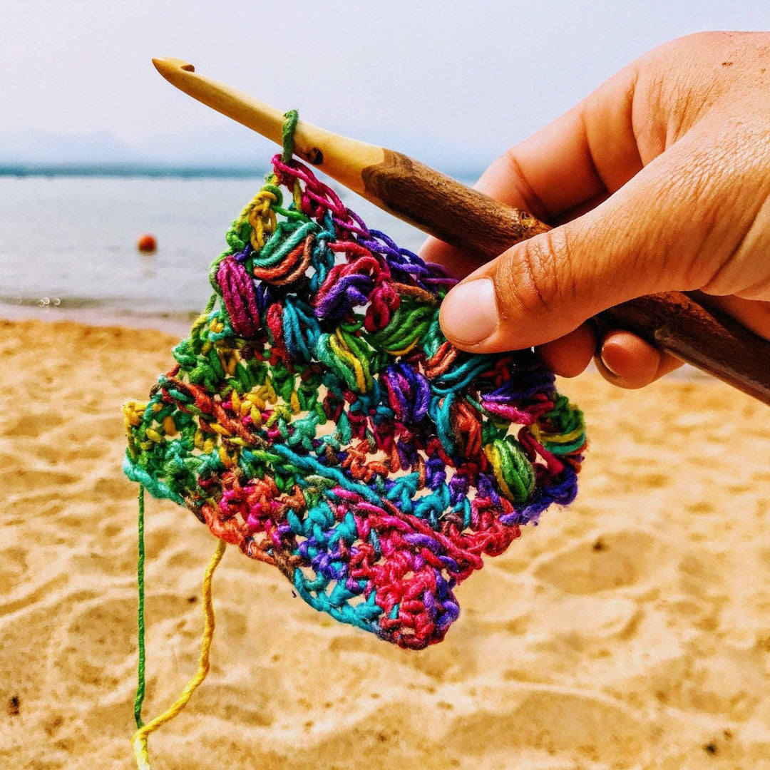 in progress image of a rainbow cowl on a crochet hook on a beach