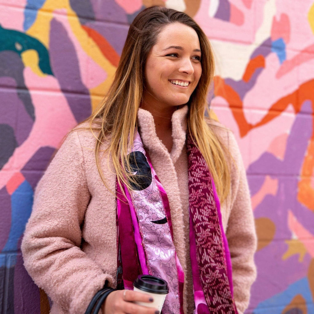 Woman standing in front of a mural, holding coffee and wearing the medley scarf around her neck