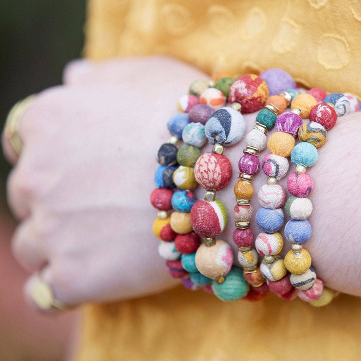 A woman's wrist with multiple different kantha bauble bracelets layered on her wrist.