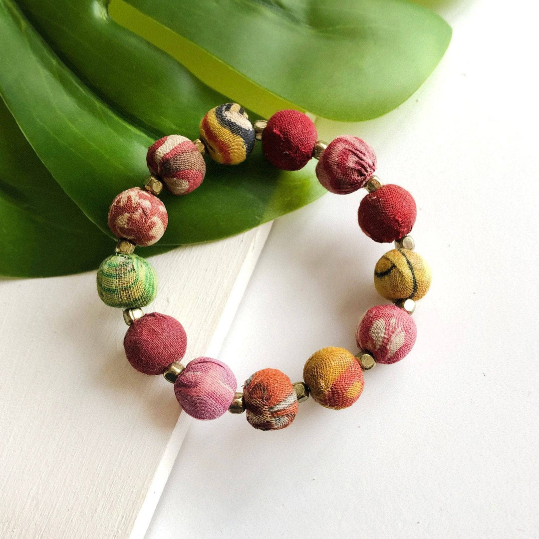 A beaded bauble bracelet made of recycled kantha on a background of white tile and greenery.