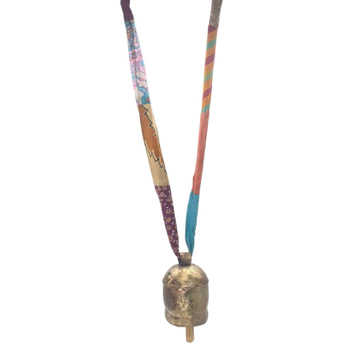 Brassy colored bell with wooden clapper, hanging from a colorful sari ribbon in front of a white background.