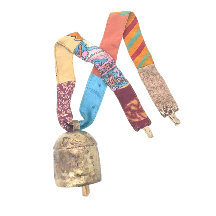 Brassy colored bell with wooden clapper, strung through colorful sari ribbon in front of a white background. 