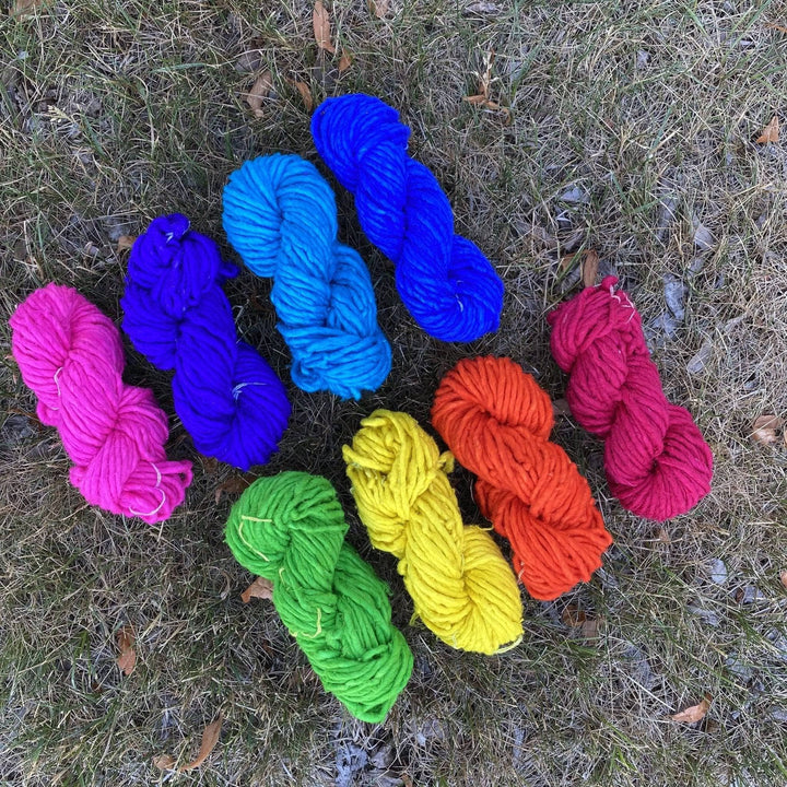 Recycled silk super bulky yarn in a rainbow of colors sitting outside on the grass.