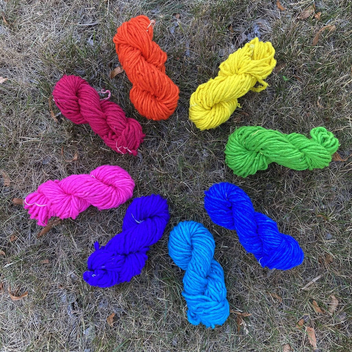 Recycled silk super bulky yarn in a rainbow of colors sitting outside on the grass.