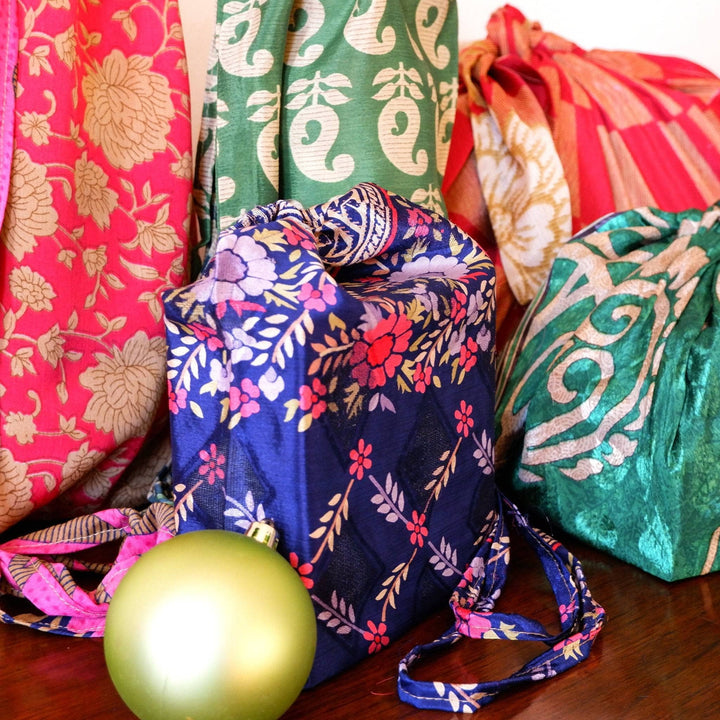 An up close shot of the presents. The smallest draw string sari silk bag is a navy blue with vibrant floral patterns on it. 