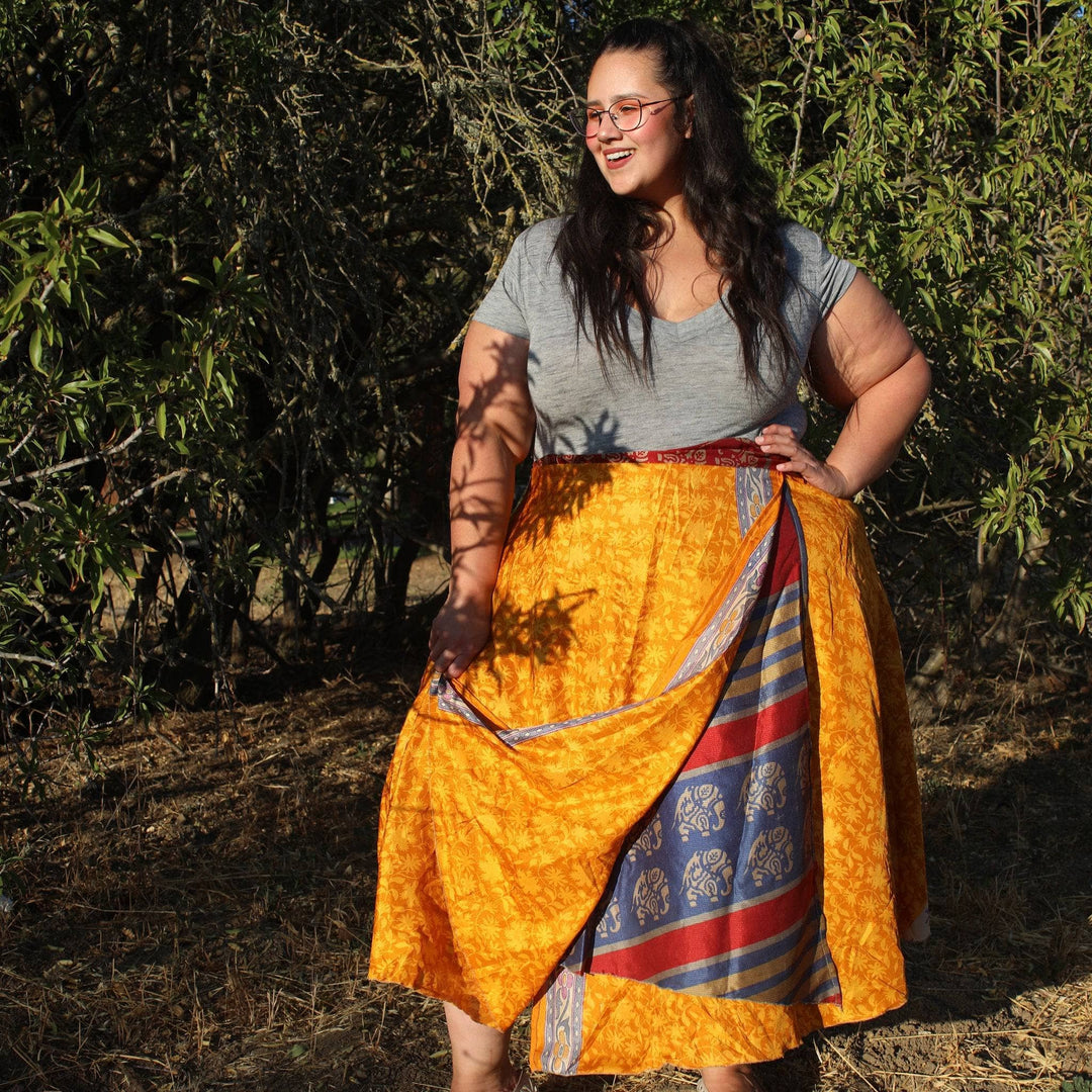 Model standing outside in front of a tree wearing a one of a kind orange tea length sari wrap skirt in goddess size.