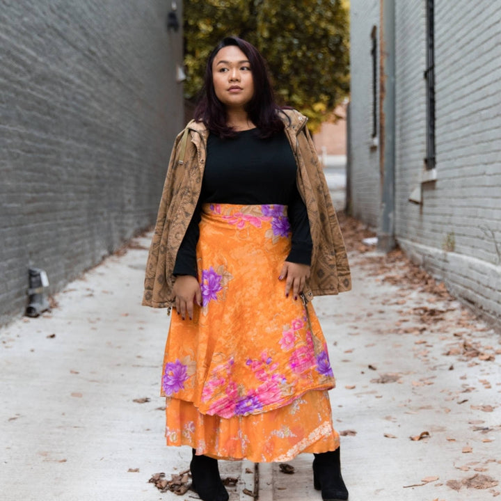 Model is wearing an orange maxi sari wrap skirt while standing in an alley. 