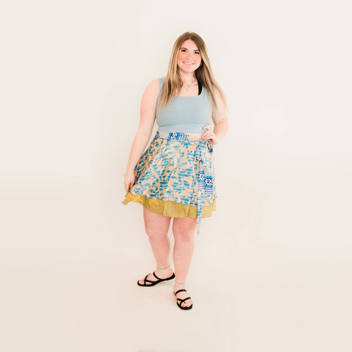 Model is wearing a plus size mini one of a kind sari wrap skirt in blue in front of a blank wall. 
