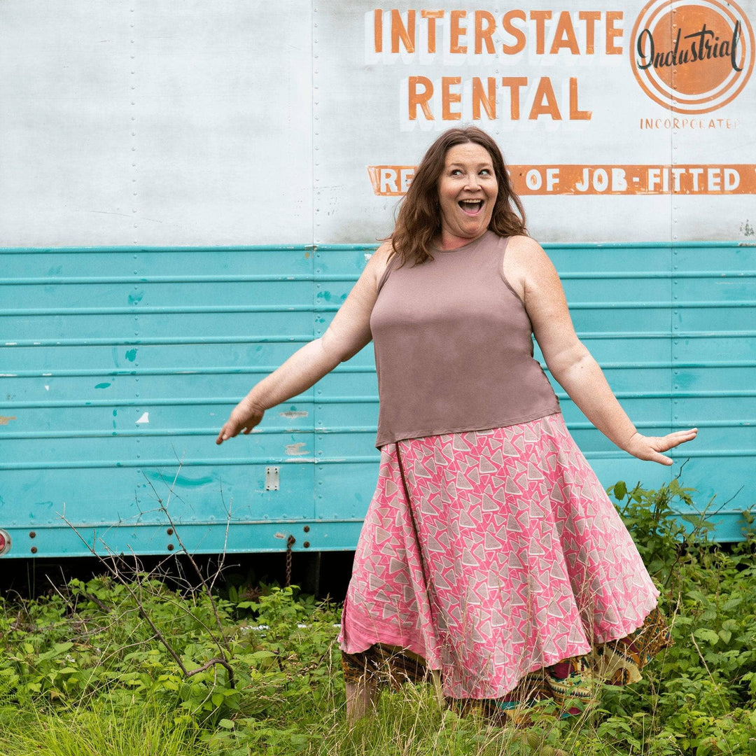 Model is standing in front of a blue trailer wearing a peachy pink sari wrap skirt. 