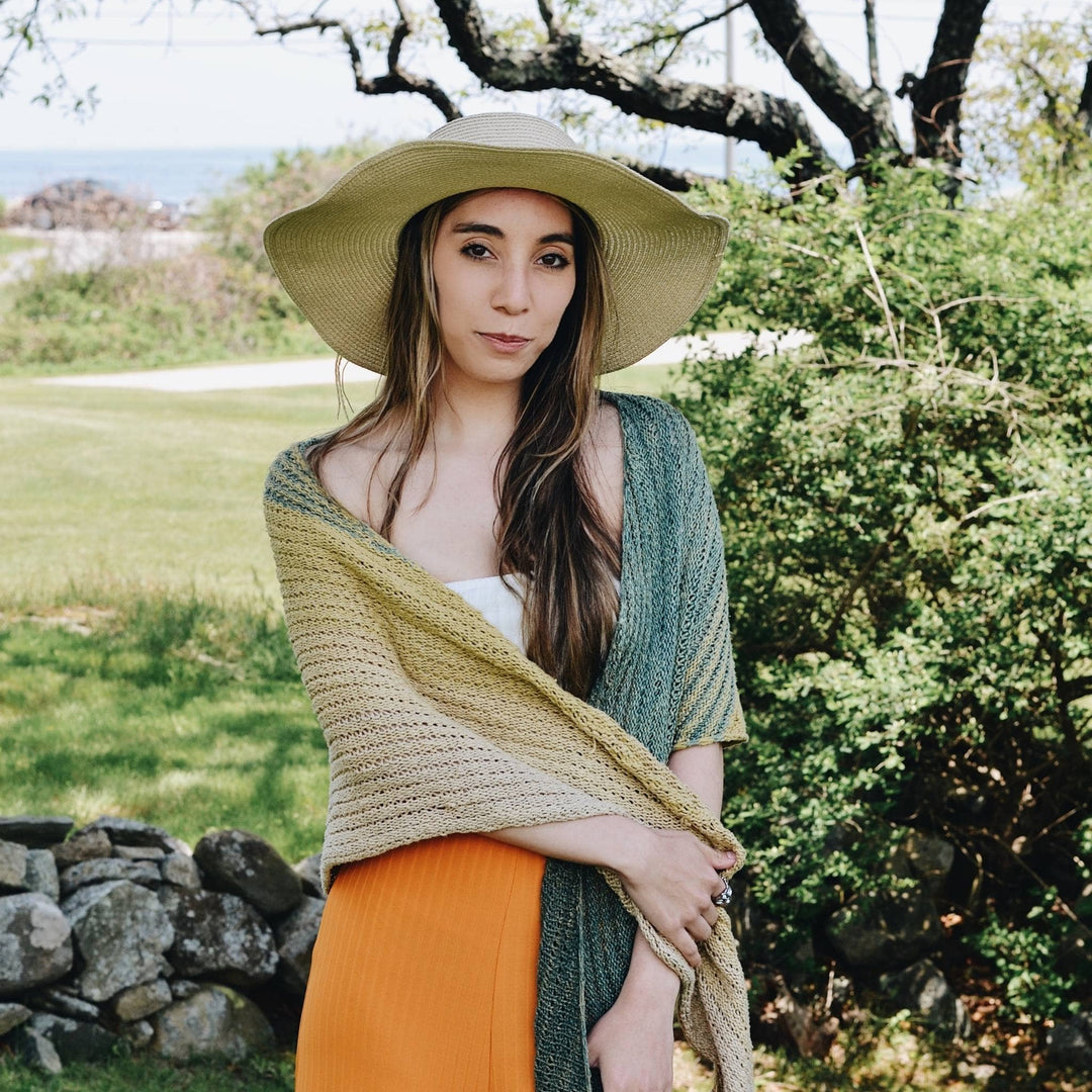 Model wearing green knit shawl with greenery in the background.