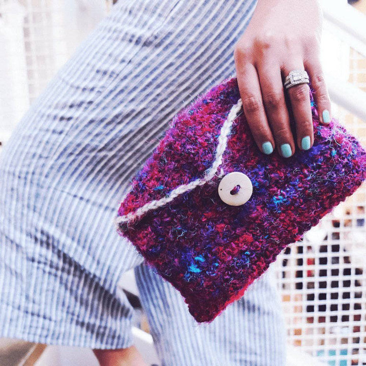 A woman holding a purple, pink and blue multicolored purse made from sari silk yarn on a white background