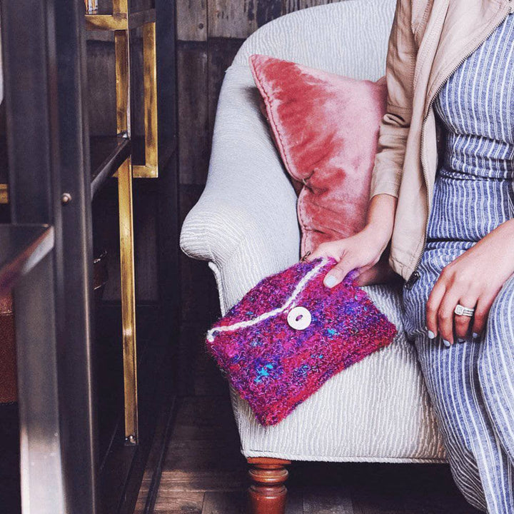 A woman holding a purple, pink and blue multicolored purse made from sari silk yarn on a white background
