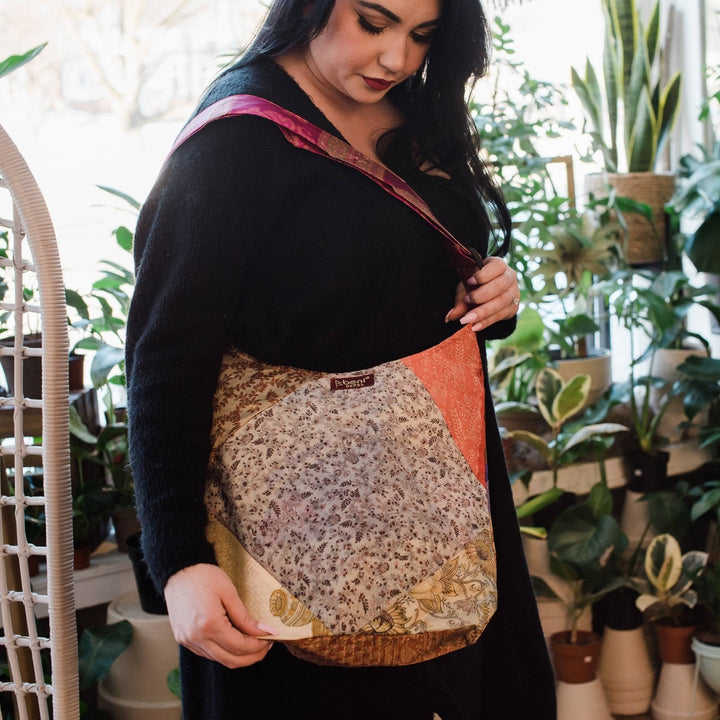 Model wearing one of a kind Sari Silk Purse with potted plants in the background. Purses are multicolor with a maroon tag that reads beni.