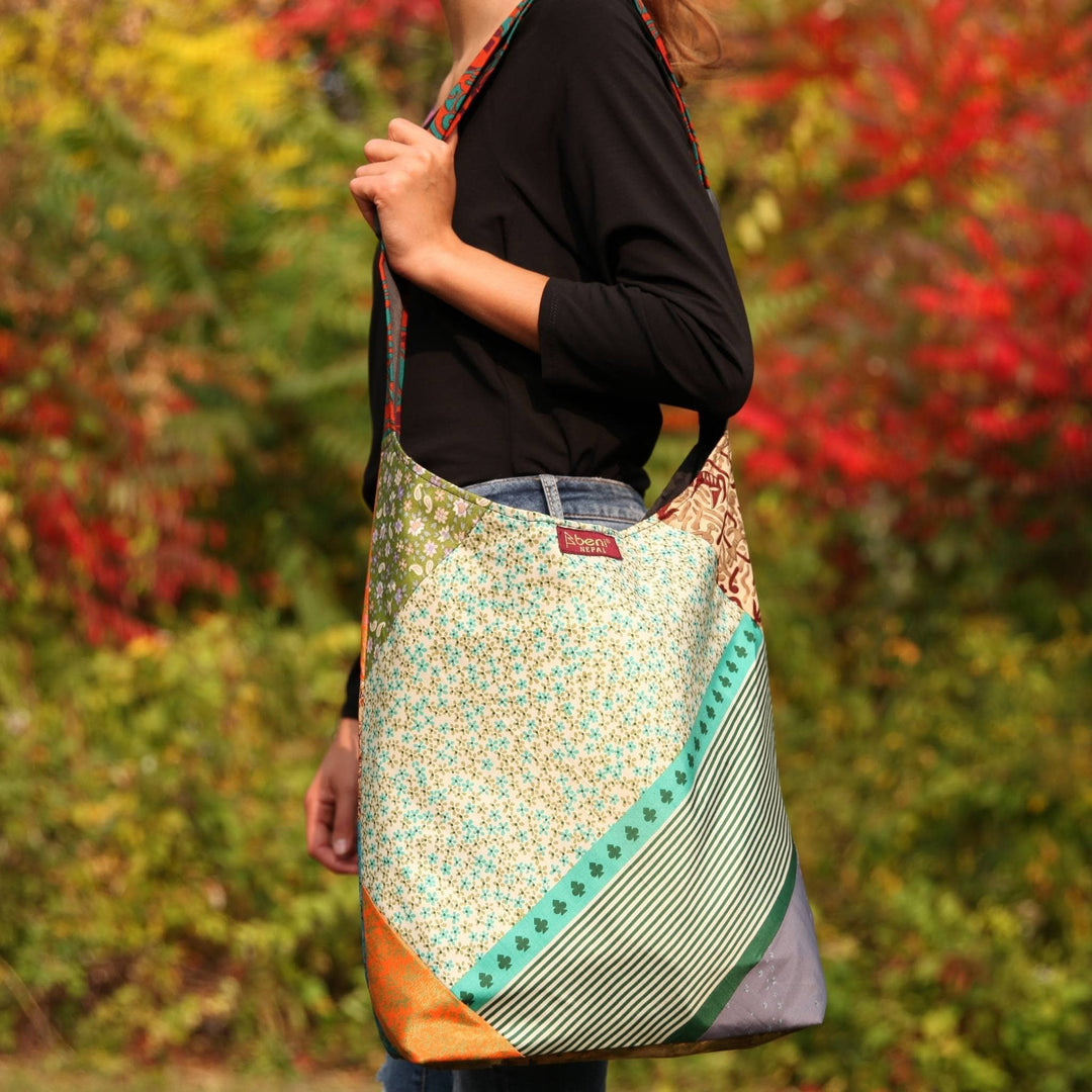 Model is standing outside in front of fall tress with a sari silk purse around her arm. 