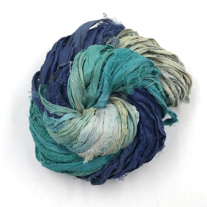 A variegated dark blue, light blue and silver skein of sari ribbon on a white background 