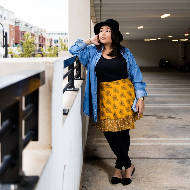 Model is in a parking garage wearing a yellow mini sari wrap skirt in size plus/xl. 