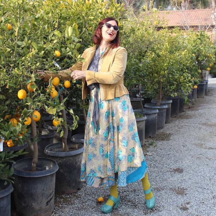 Artist Deanna Bowers is standing outside in front of lemon trees wearing a tea length sari wrap skirt with a blue floral pattern.